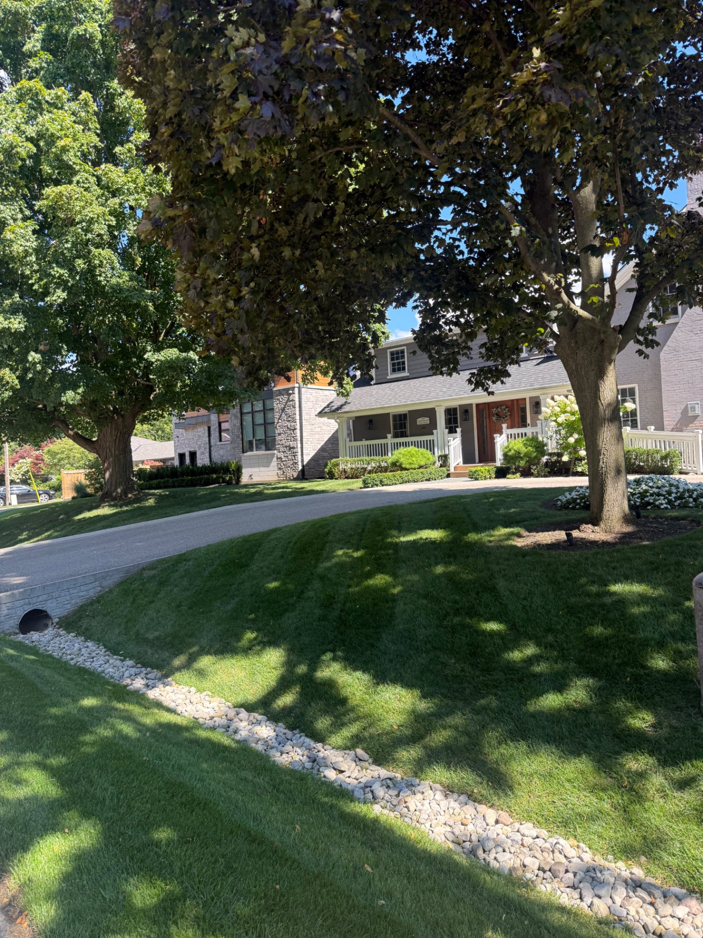 Manicured front lawn with river-rock swale and mature shade trees
