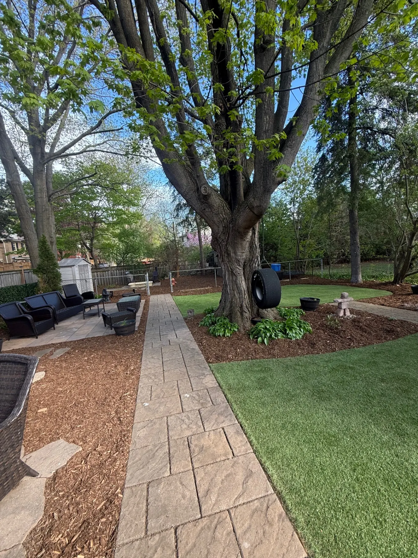 Backyard with artificial turf, paver walkway, and mulched beds